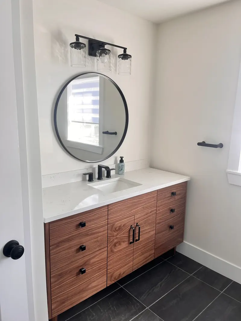 A bathroom vanity with a round mirror and wood drawers